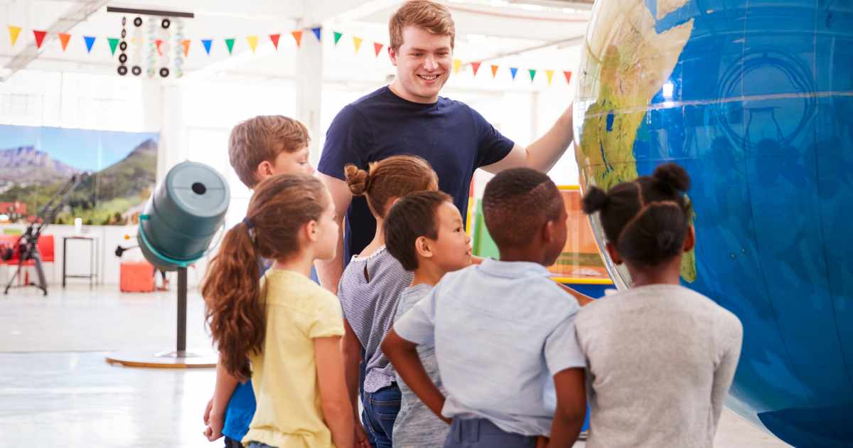 A group of children with a young male science communicator looking at a large model globe
